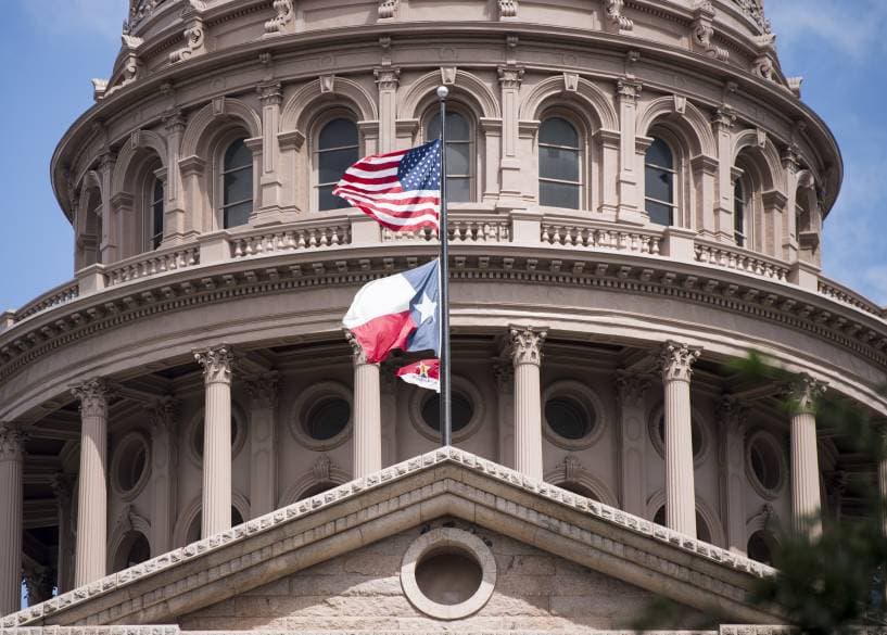 American and state flags flying in front of a state capitol dome